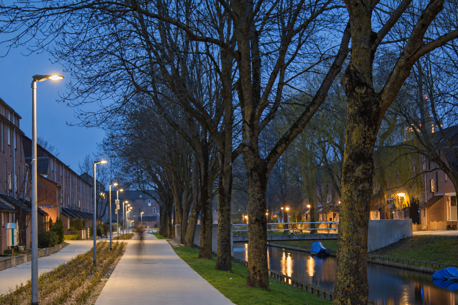Outdoor luminaires illuminating a canal-side pedestrian route in Europe at dusk